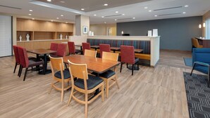 A modern dining area with wooden tables and chairs, a counter with a television, and a seating area with colorful cushions. - TownePlace Suites by Marriott Niceville Eglin AFB Area (Niceville)