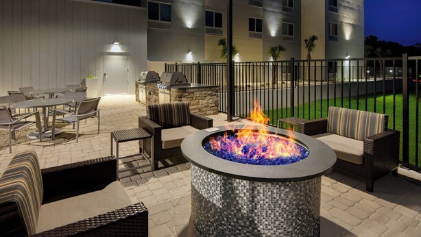 An outdoor patio with a fire pit, seating, and a view of a building in the background. - TownePlace Suites by Marriott Niceville Eglin AFB Area (Niceville)
