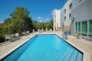 Una piscina rectangular con borde de azulejos, rodeada por una solana pavimentada. Hay varias sillas de descanso y una pequeña mesa en la solana.