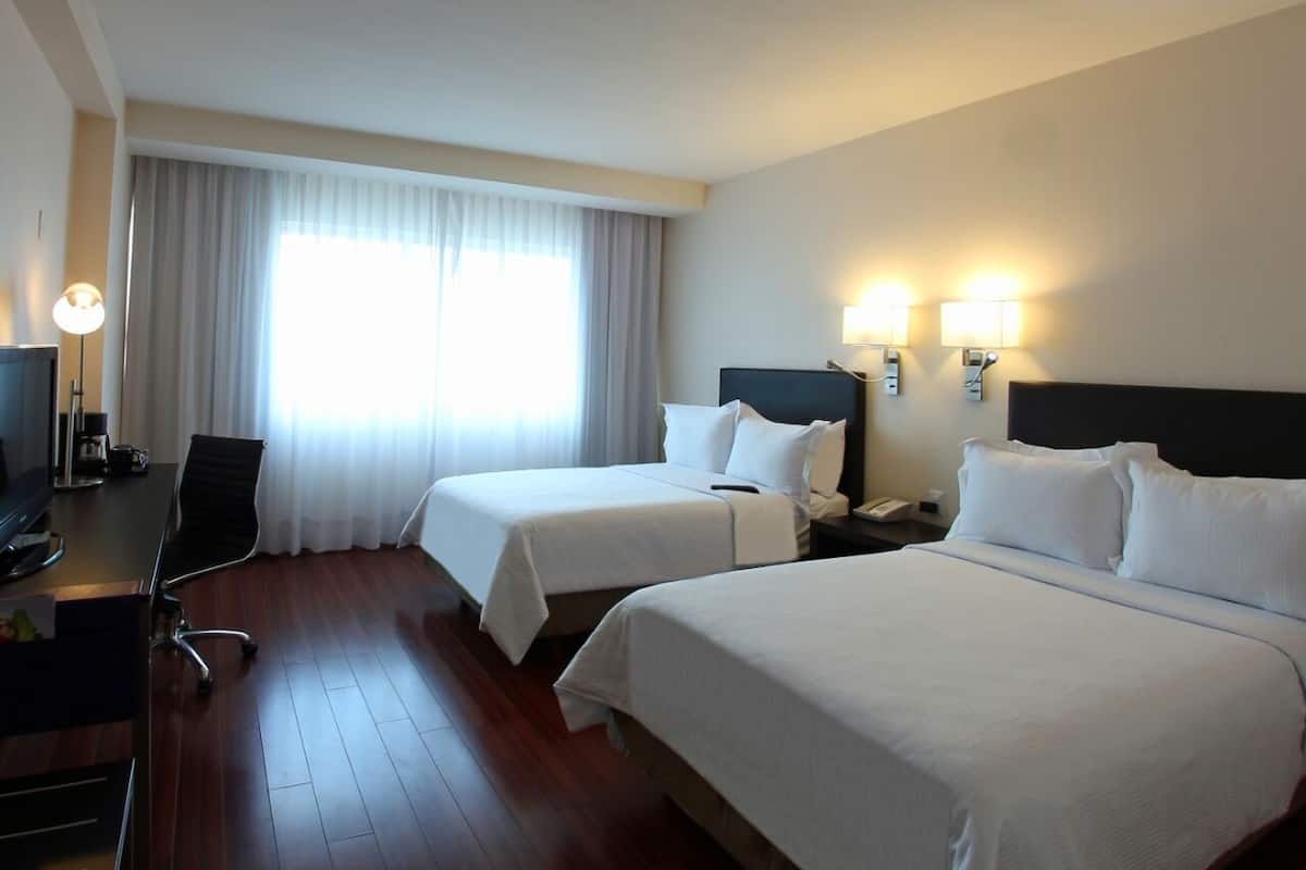 A hotel room with two beds, a desk with a computer, a chair, and a TV.