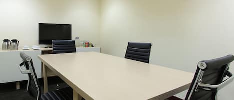 A conference room with a long table, four chairs, a television, and a small table with cups and a coffee maker.