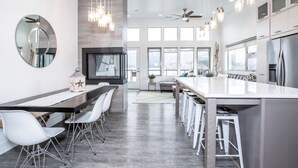 Una cocina moderna con una isla grande, taburetes blancos de bar, un espejo redondo e iluminación colgante.