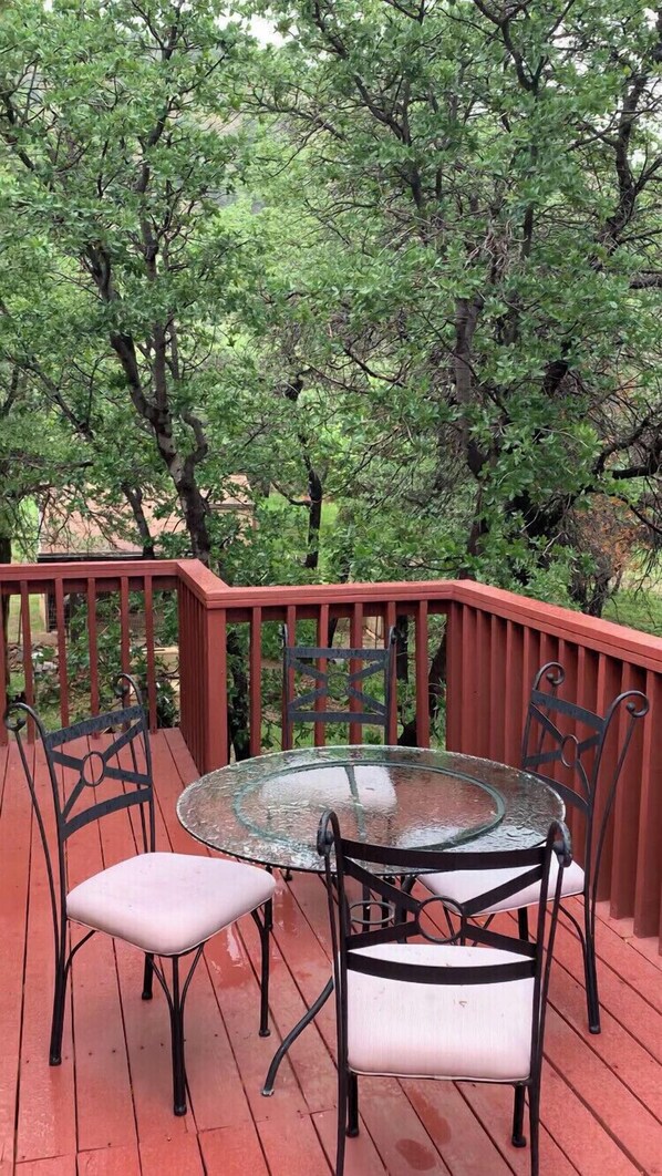 Relax on the deck with a glass-top table and four chairs, surrounded by lush greenery.