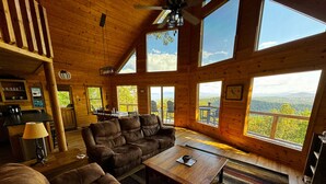 A cozy cabin interior with a large sofa, a coffee table, and a dining area with a view of the mountains. - Best view in Georgia. Unbelievably peaceful. Amazing night sky. (Morganton)