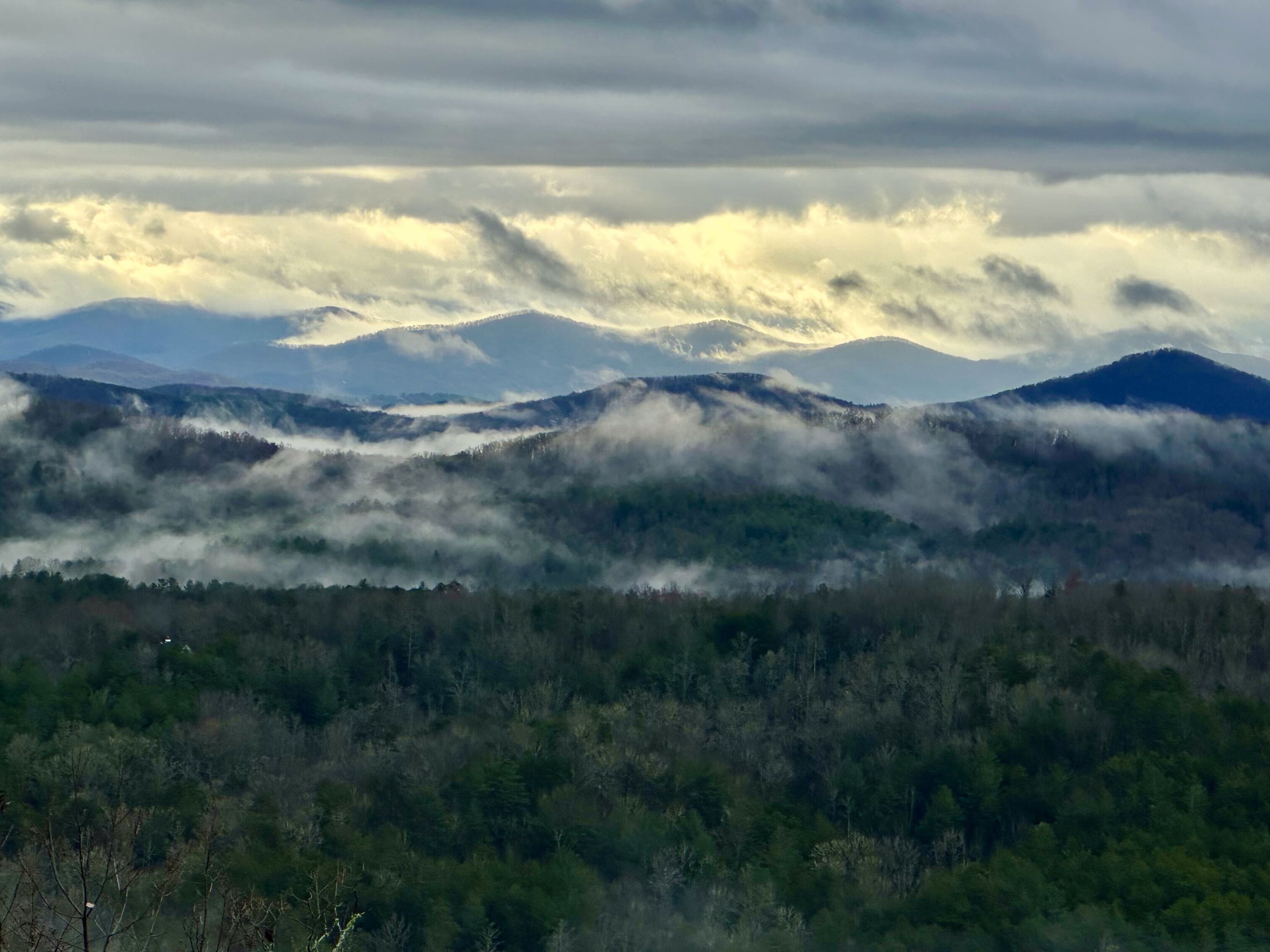 A mountainous landscape with forested valleys and a cloudy sky.