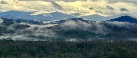 A mountainous landscape with forested valleys and a cloudy sky.