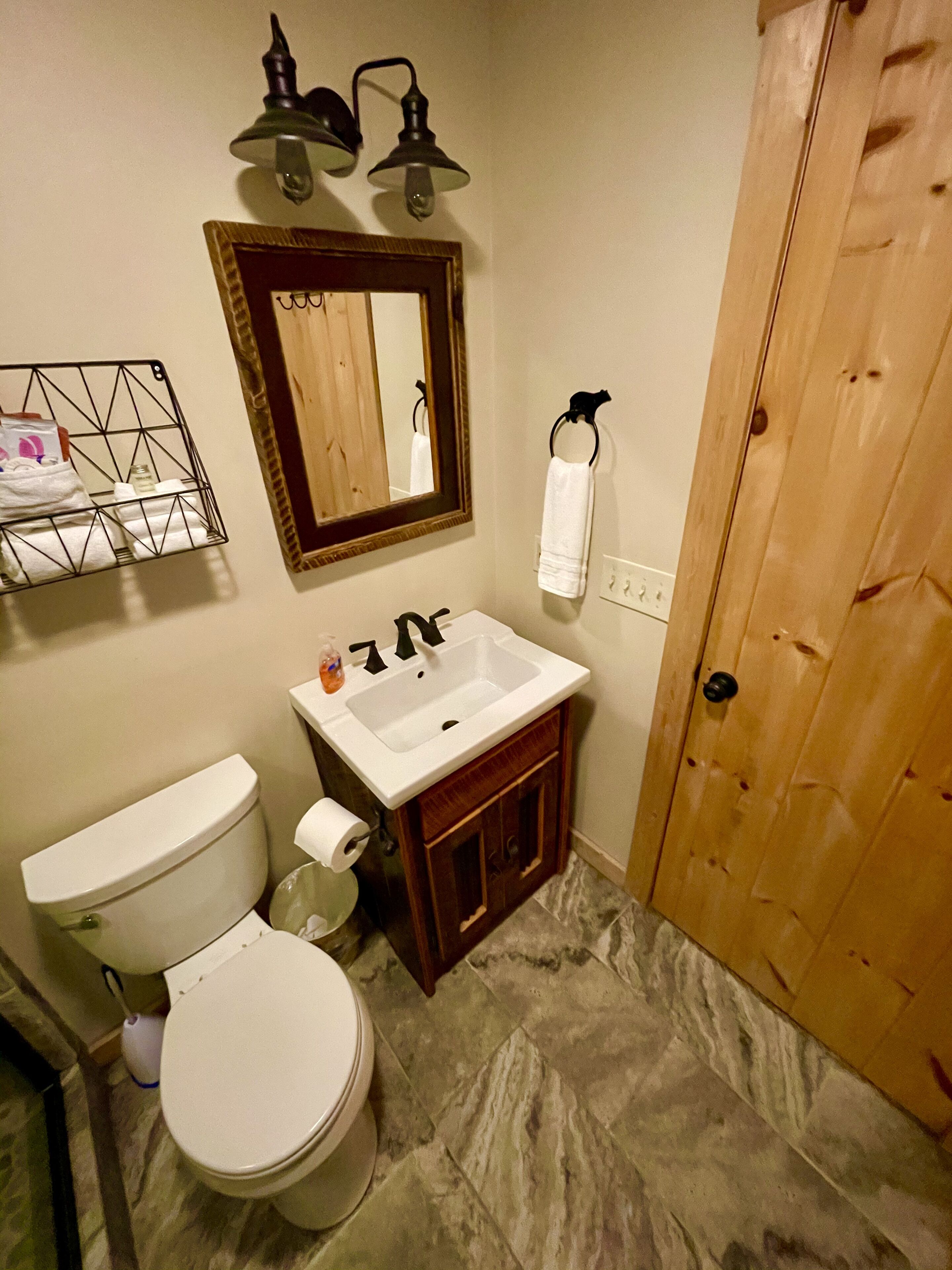 Une salle de bain équipée de toilettes, d’un lavabo, d’un miroir et d’une porte en bois.