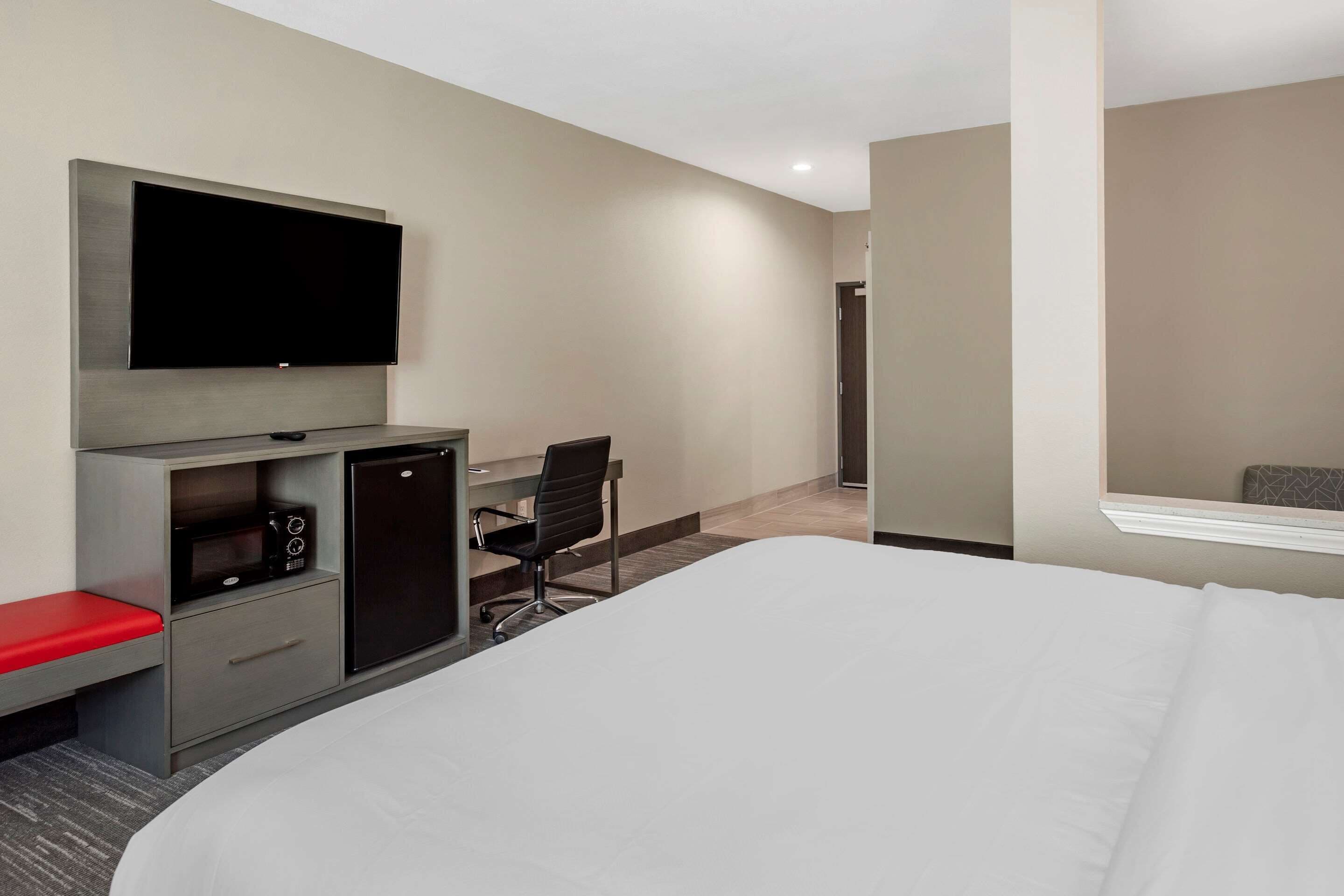 Habitación de hotel con una cama grande, un escritorio con silla, televisión, microondas y refrigerador.