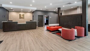 A modern reception area with a reception desk, a seating area with red and white furniture, and a textured wall with a logo. - Comfort Inn & Suites Olive Branch Old Towne (Olive Branch)