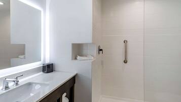 Un baño con un espejo grande, un lavabo, un perchero para toallas y una ducha con puerta de cristal.