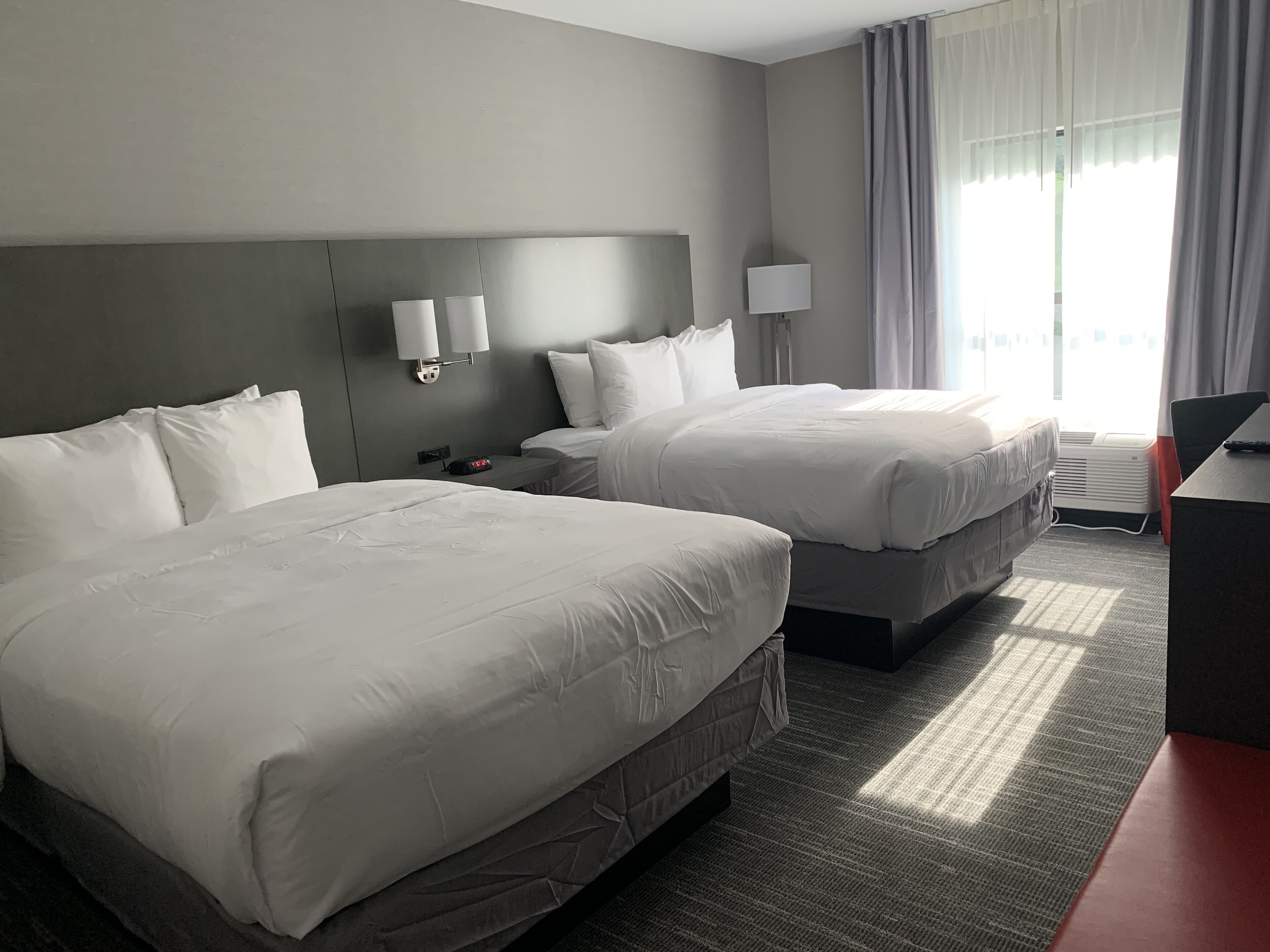 Une chambre d’hôtel avec deux lits, un bureau, une lampe et une fenêtre avec des rideaux.