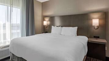 Una habitación de hotel con una cama grande, dos mesitas de noche con lámparas, una ventana con cortinas y una lámpara de pared.