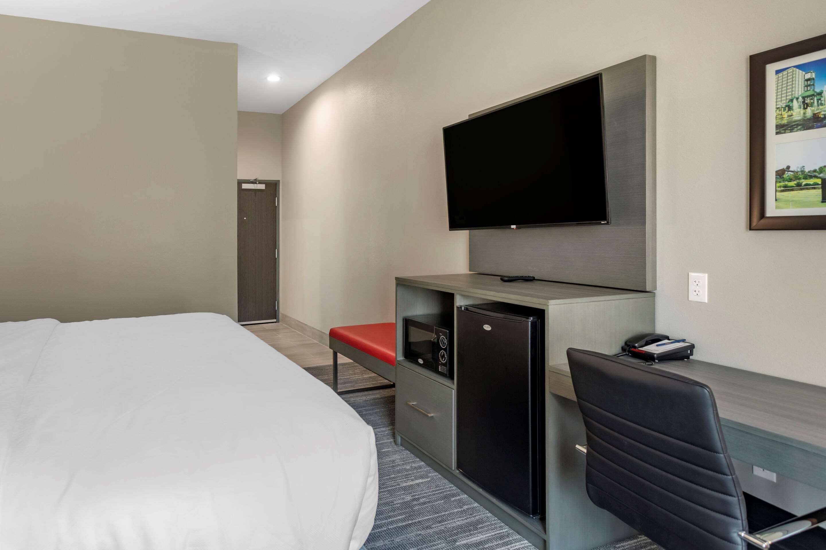 A hotel room with a bed, a desk with a computer, a TV, and a small refrigerator.