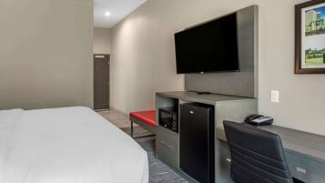 A hotel room with a bed, a desk with a computer, a TV, and a small refrigerator.