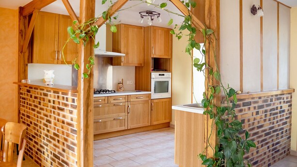 A kitchen with wooden cabinets, a gas stove, an oven, and a brick wall.