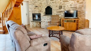A living room with a stone wall, a fireplace, a television, and a staircase.