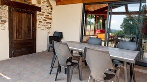 A patio with a table and chairs, a wooden door, and a view through large windows.