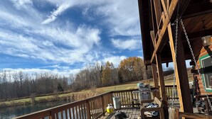 A wooden deck with a view of a lake, a grill, and outdoor seating. - Private Log Cabin Rental (Drayton Valley)