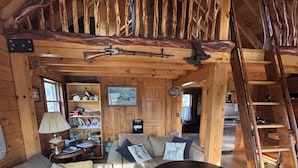 A cozy log cabin interior with a wooden staircase, a sofa set, a coffee table, and a bookshelf. - Private Log Cabin Rental (Drayton Valley)