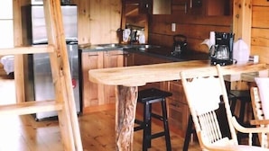 A wooden cabin interior with a kitchen area, a dining table with chairs, and a ladder. - Private Log Cabin Rental (Drayton Valley)