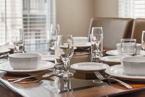 A dining table set with white plates, bowls, and clear glasses, with a reflective surface and a view of the outside through large windows. - Walk-in Golf Condo feat. All-Season Sunroom with Course View (Branson)