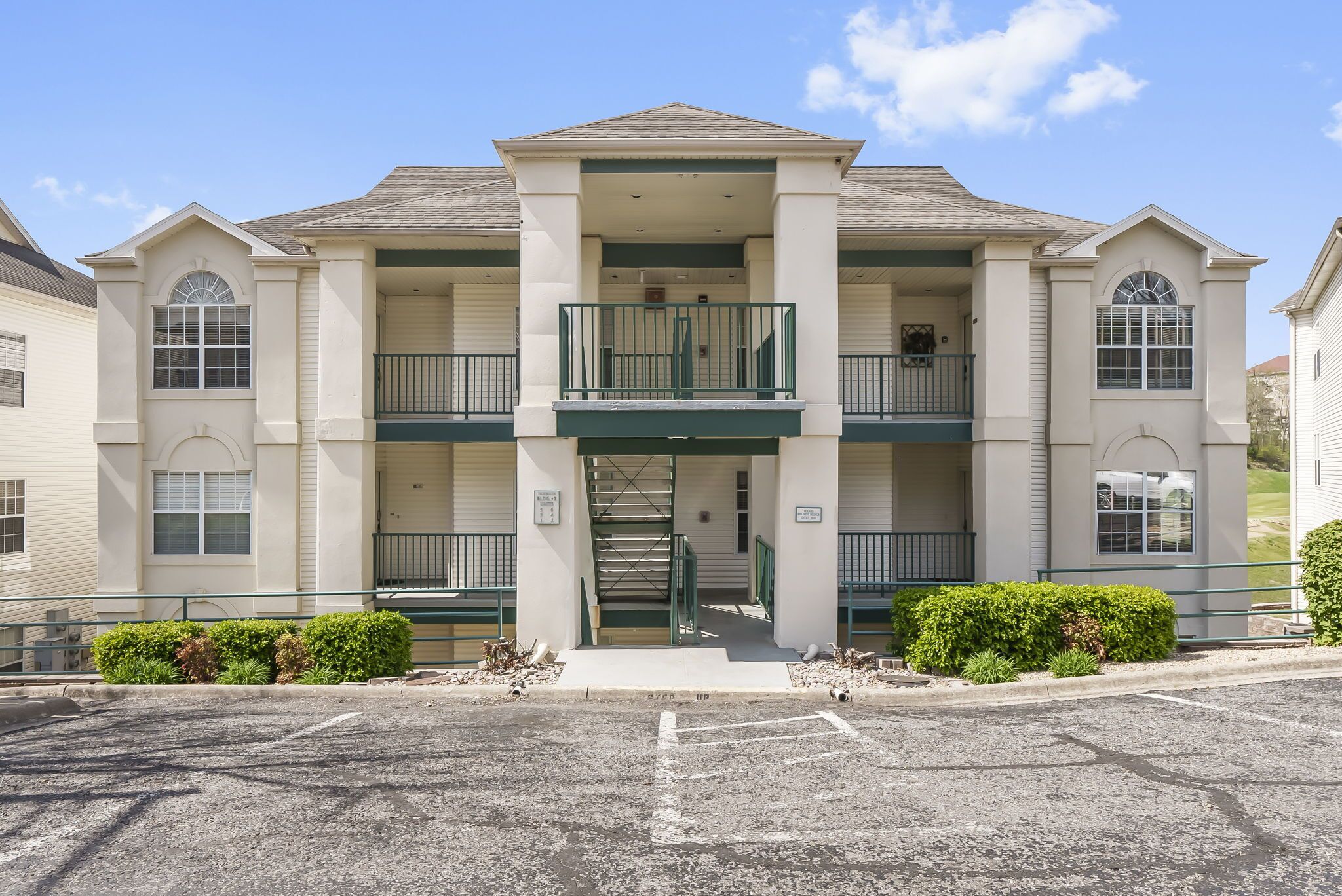 A two-story building with a central entrance, a balcony on the second floor, and a parking lot in front.