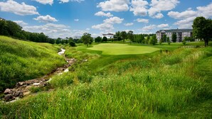 Un campo de golf con un arroyo, un club de campo y edificios residenciales al fondo.