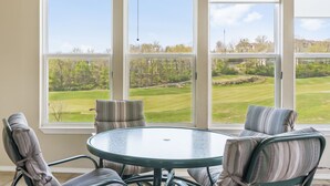 Una habitación con una mesa redonda de vidrio y sillas a rayas, ventanas amplias con vistas a un campo de golf.