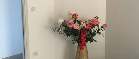 A hallway with a wall-mounted clock, a vase with flowers, and a door.