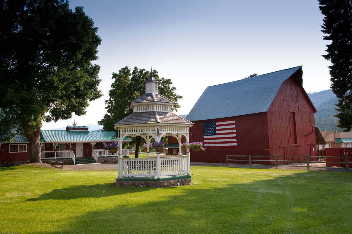 A gazebo with a white picket fence, a red barn, and an American flag in the background.