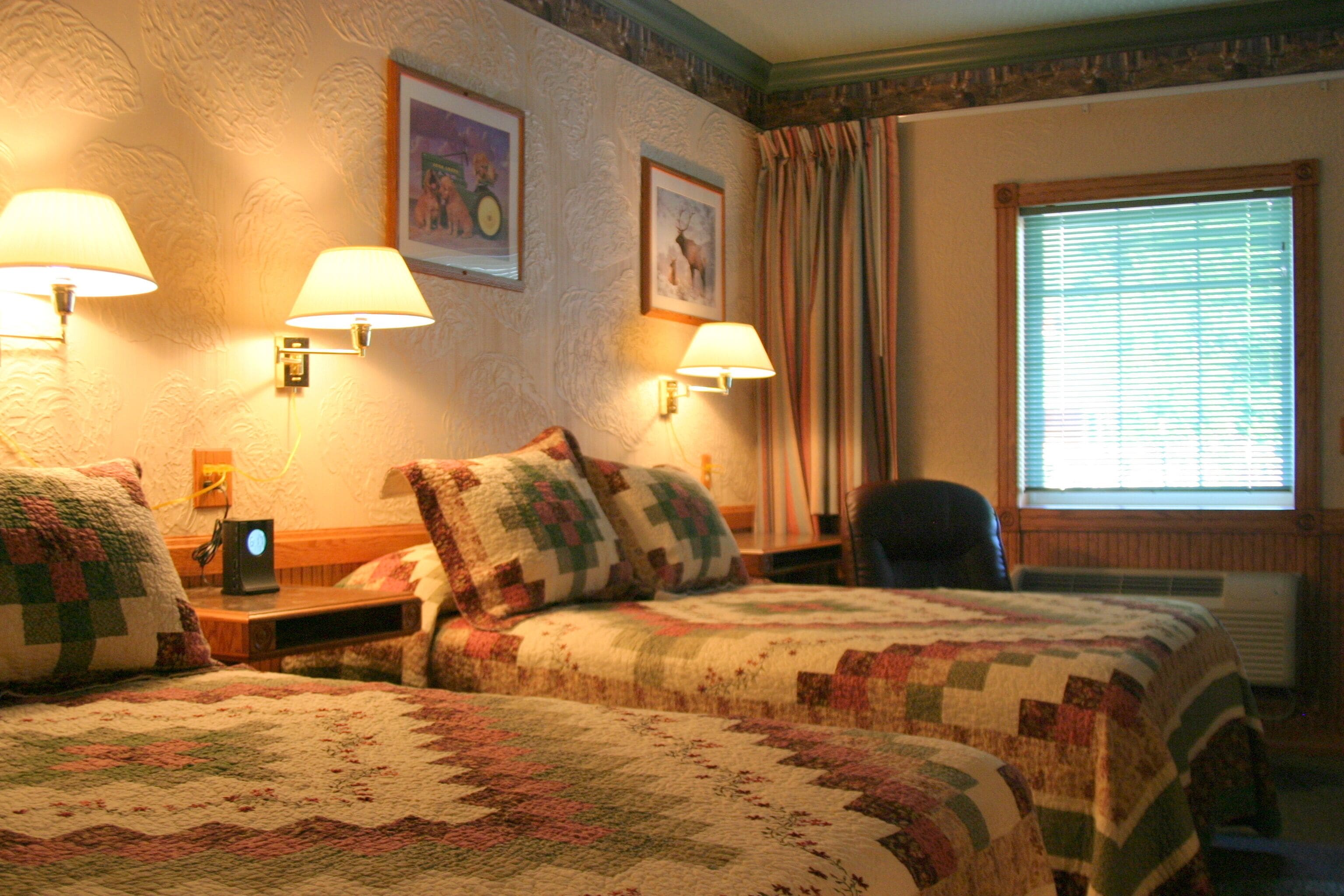 Une chambre d’hôtel avec deux lits, chacun recouvert d’une courtepointe, deux lampes fixées au mur et un tableau encadré au-dessus des lits.