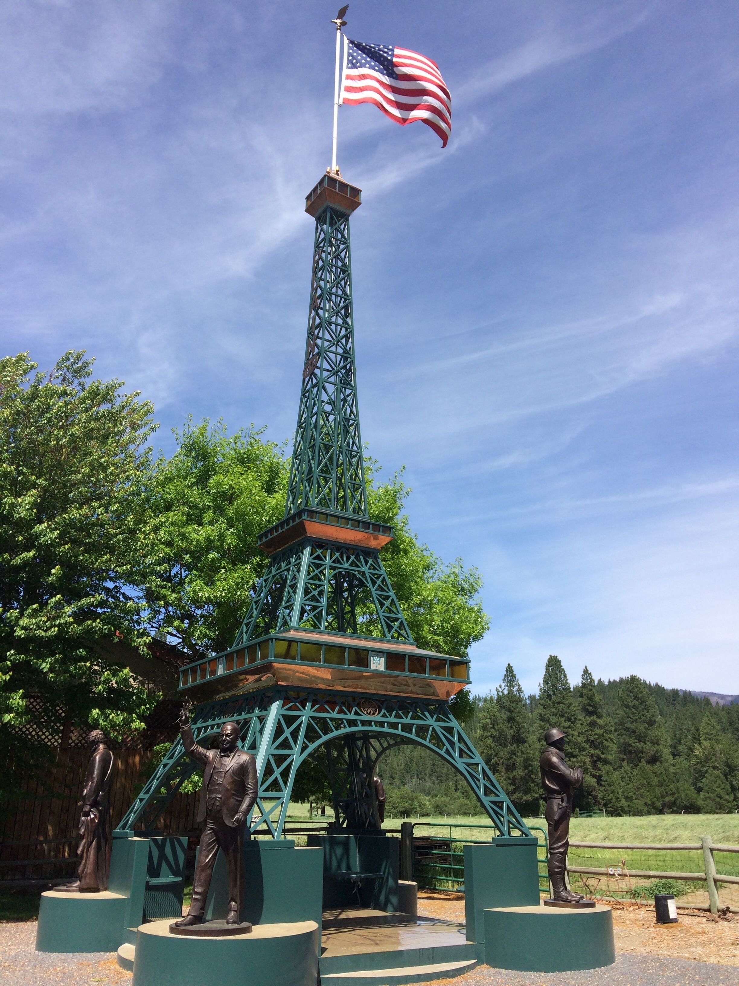 A replica of the Eiffel Tower with an American flag, surrounded by statues and greenery.