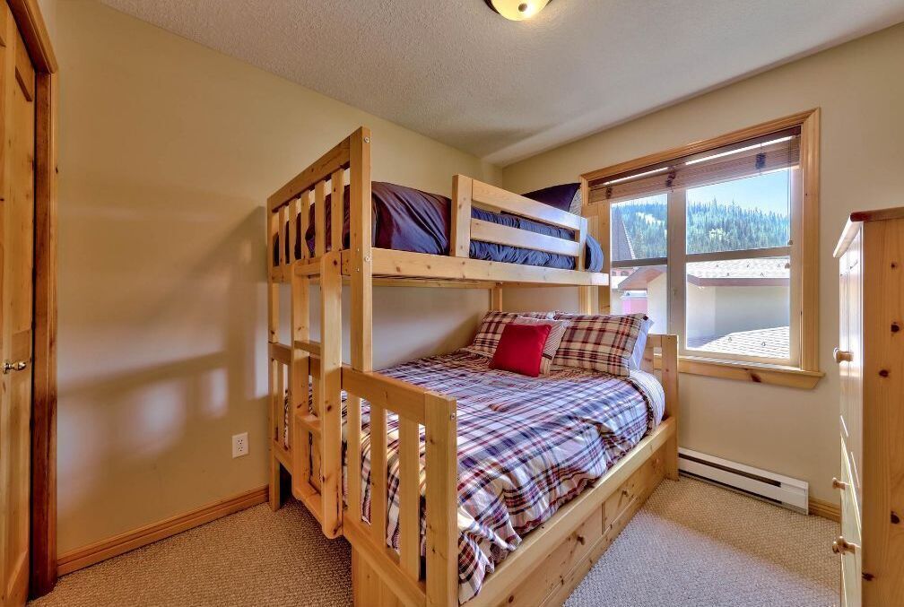A bunk bed room with a window view of a forest.