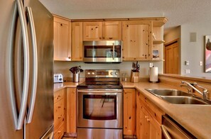 A kitchen with wooden cabinets, stainless steel appliances, a microwave, oven, and a sink. - Perfect family vacation home  4 bedroom w/ private hot tub (Sun Peaks)