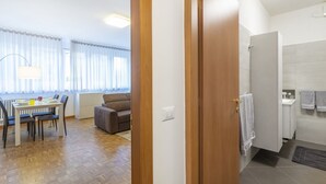 Ein modernes Wohnzimmer mit Esstisch, Sofa und Blick durch eine Tür auf ein Badezimmer mit Handtuchhalter.