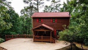 A wooden cabin with a porch, surrounded by trees.