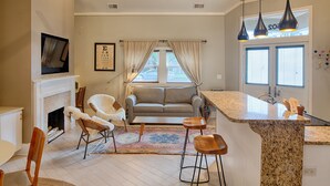 A living room with a fireplace, a sofa, and a dining area with chairs. There is a kitchen with a bar and pendant lights. - Romantic Cottage in Savannah's Beautiful Historic District! (Savannah)
