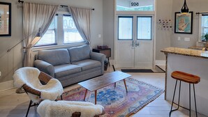 A living room with a grey sofa, a white furry chair, a wooden coffee table, and a patterned rug. - Romantic Cottage in Savannah's Beautiful Historic District! (Savannah)