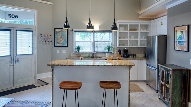 A modern kitchen with a central island, pendant lights, and a refrigerator. - Romantic Cottage in Savannah's Beautiful Historic District! (Savannah)