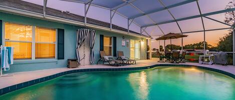 A swimming pool with lounge chairs and umbrellas, surrounded by a covered patio area.