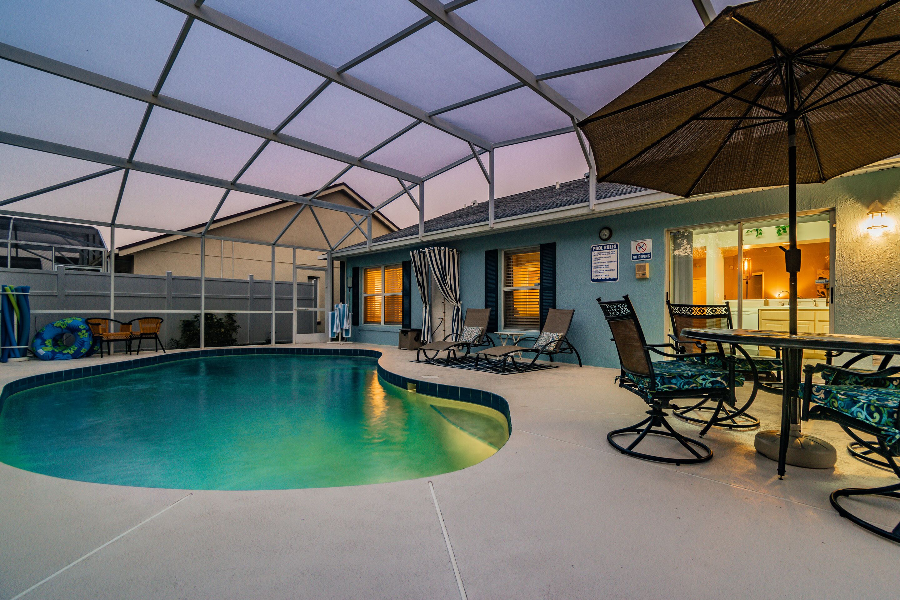 An indoor swimming pool with a covered patio area, lounge chairs, and a table with chairs.