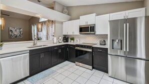 A modern kitchen with dark cabinets, stainless steel appliances, and a tiled backsplash. - Near Theme Parks! In-Ground 3 BR Pool Home, Sleeps 7, Total Privacy! (Kissimmee)