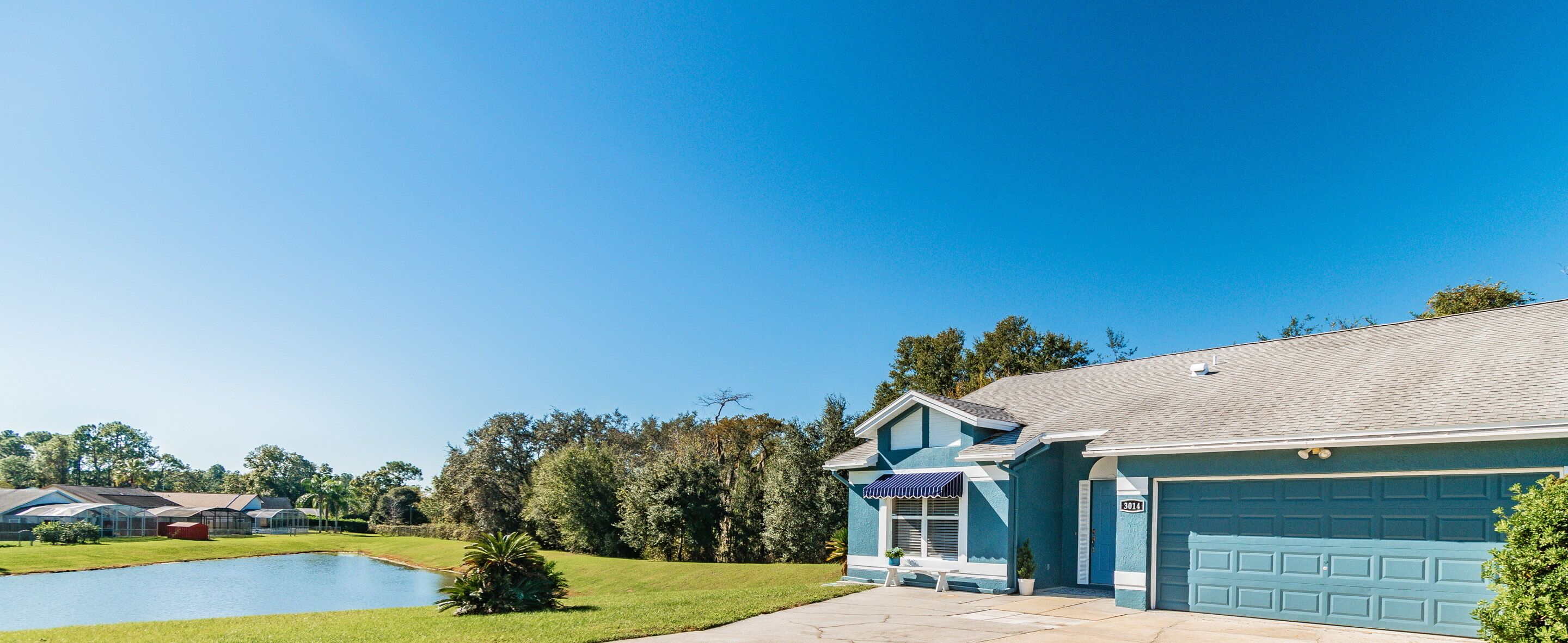 A residential house with a blue garage, a small front yard, and a pond.