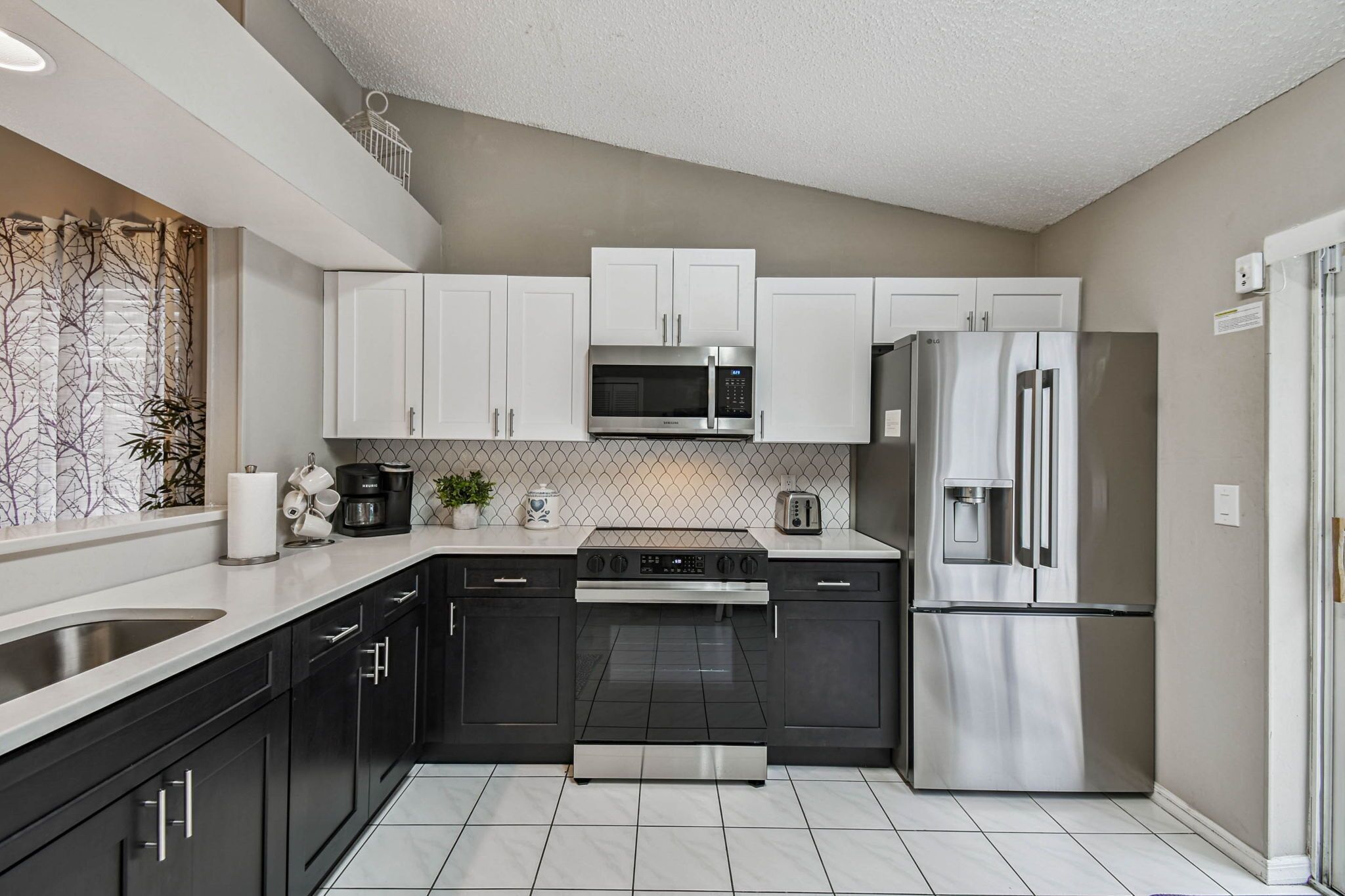 A modern kitchen with black and white cabinetry, stainless steel appliances, and a tiled backsplash.