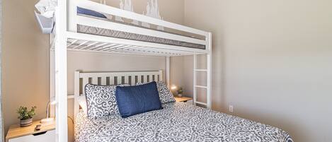 A bunk bed with a patterned bedspread, a bedside table with a lamp, and a small plant.