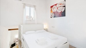 A white bedroom with a bed, a window, an air conditioner, and a painting on the wall. - GuestHost - Functional 35sqm apartment, well furnished, that can accommodate up to 4 people. Located on the third floor, without lift, of an historic Florentine building few steps away from Palazzo Medici Riccardi and 3 minutes on foot from the Duomo. Th (Firenze)