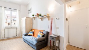 A living room with a sofa, a small table, a radiator, a door, and a window. - GuestHost - Functional 35sqm apartment, well furnished, that can accommodate up to 4 people. Located on the third floor, without lift, of an historic Florentine building few steps away from Palazzo Medici Riccardi and 3 minutes on foot from the Duomo. Th (Firenze)