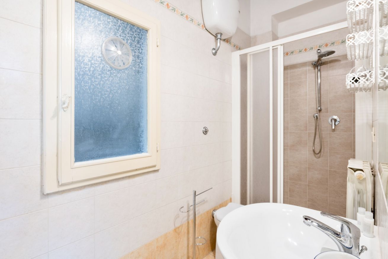 A bathroom with a toilet, sink, shower, and a window with a frosted glass door.