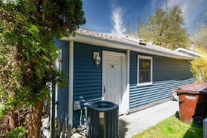Simple, single-story building with a white door and small window above, surrounded by trees.