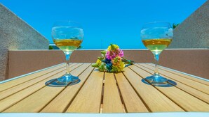 Twee wijnglazen met een bloemstuk op een houten tafel voor een helderblauwe lucht.